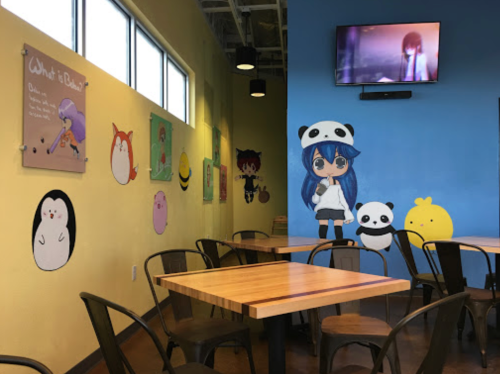 Colorful café interior with cartoon wall art, wooden tables, and a TV displaying an animated character.